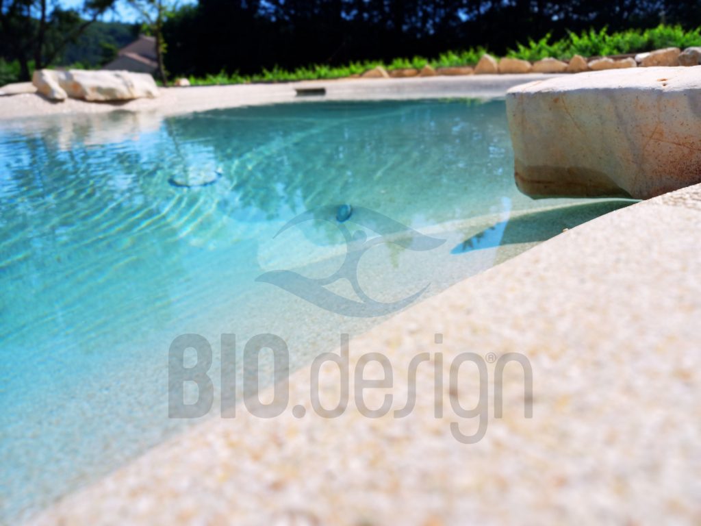 Bord de piscine lagon Biodesign avec finition sable et margelle en pierre naturelle – conception Florasol.