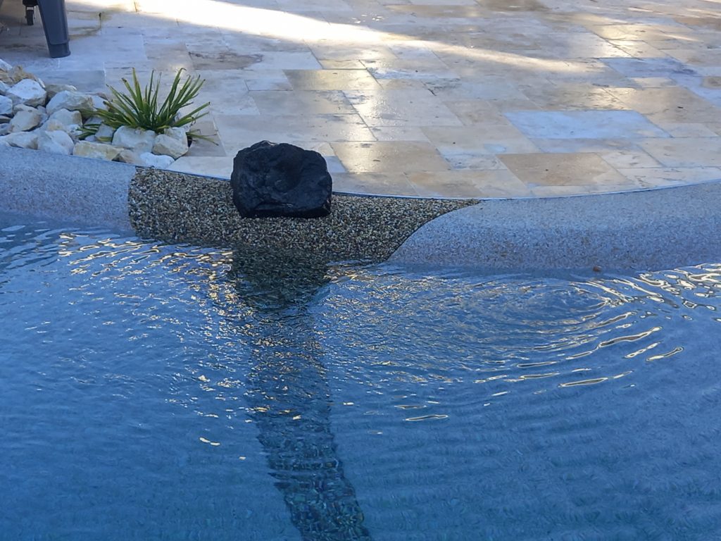 Détail des finitions d'un lagon Bio.design avec plage immergée et terrasse en pierre naturelle