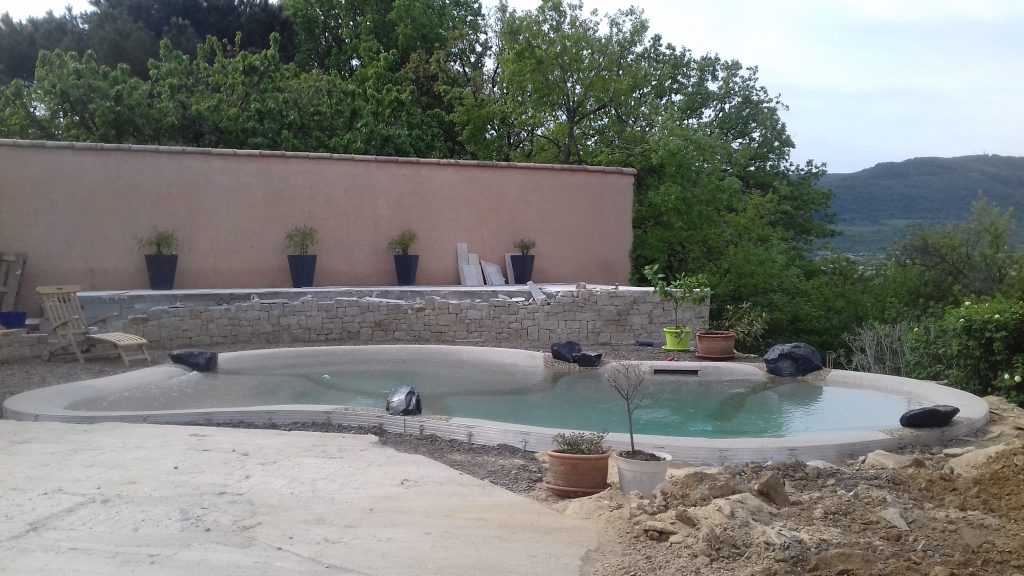 Lagon Bio.design en cours de finition avec mur de soutènement habillé en pierres sèches et terrasse surélevée