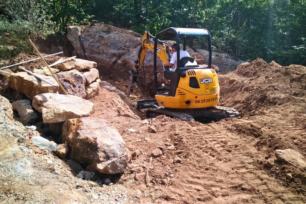 Mini-pelle réalisant le terrassement d'une piscine lagon sur terrain rocheux naturel en Ardèche
